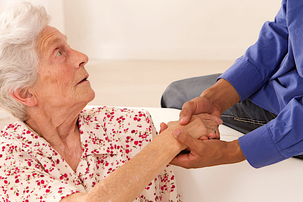 Caregiver holding elderly lady's hands.